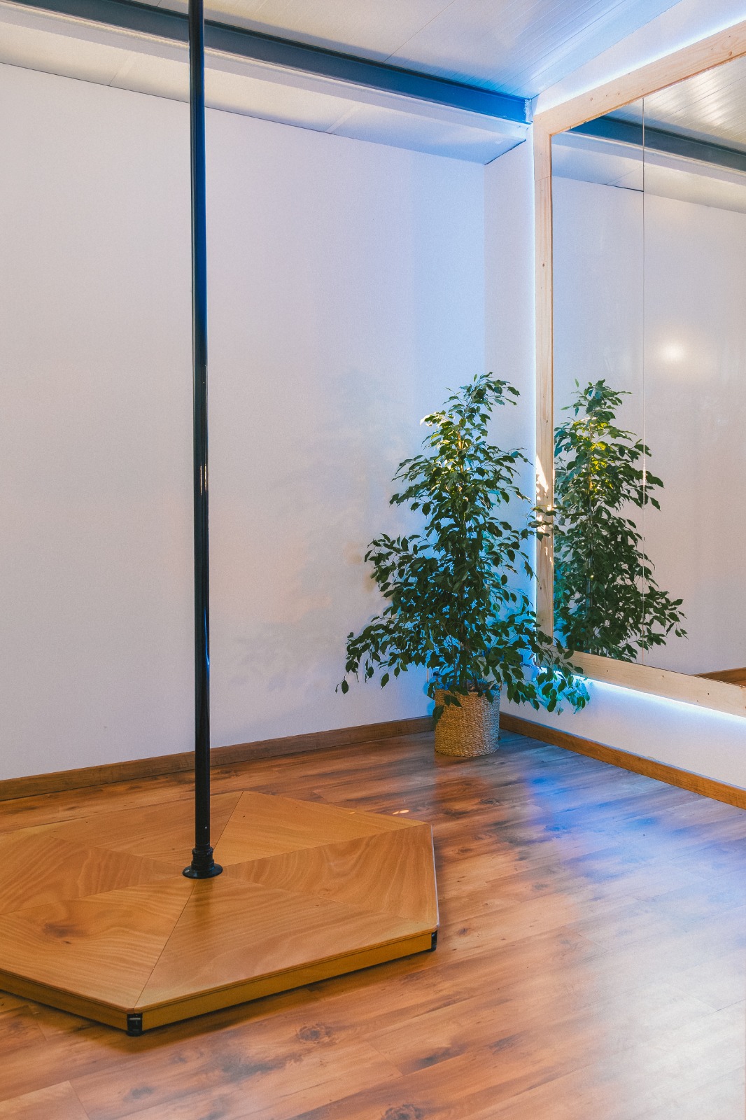 Plateforme en bois et barre de pole dance noire devant un grand miroir lumineux
